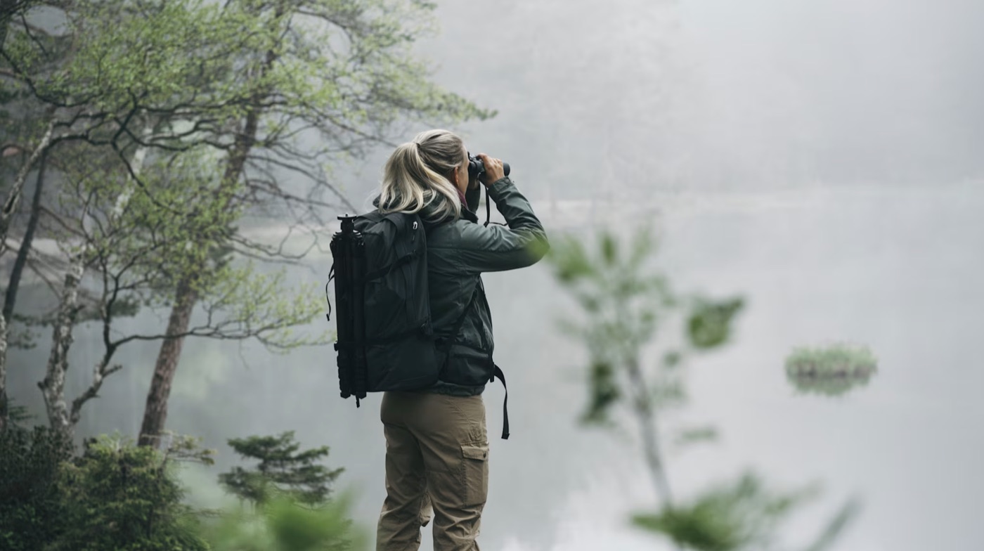Eine Person beobachtet mit einem Fernglas die Natur. Standbild aus dem Jubiläumsfilm für Swarovski Optik.